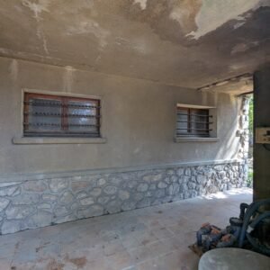 Mur extérieur en pierre et enduit, avec des fenêtres grillées et un éclairage extérieur.