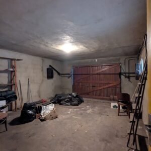 Sous-sol sombre et encombré avec des meubles et des déchets, nécessitant une rénovation.