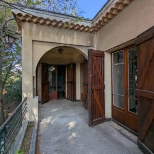 Entrée d'une maison avec un porche en pierre et des portes en bois ouvertes.