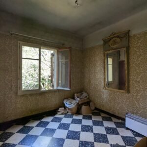 Une pièce délabrée avec un motif de carrelage noir et blanc, un miroir et un papier peint usé.