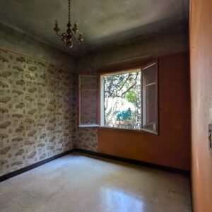Une pièce délabrée avec un papier peint vintage et une fenêtre donnant sur un jardin.