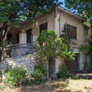 Maison de campagne en pierre avec toit en tuiles, entourée de verdure et d'arbres.
